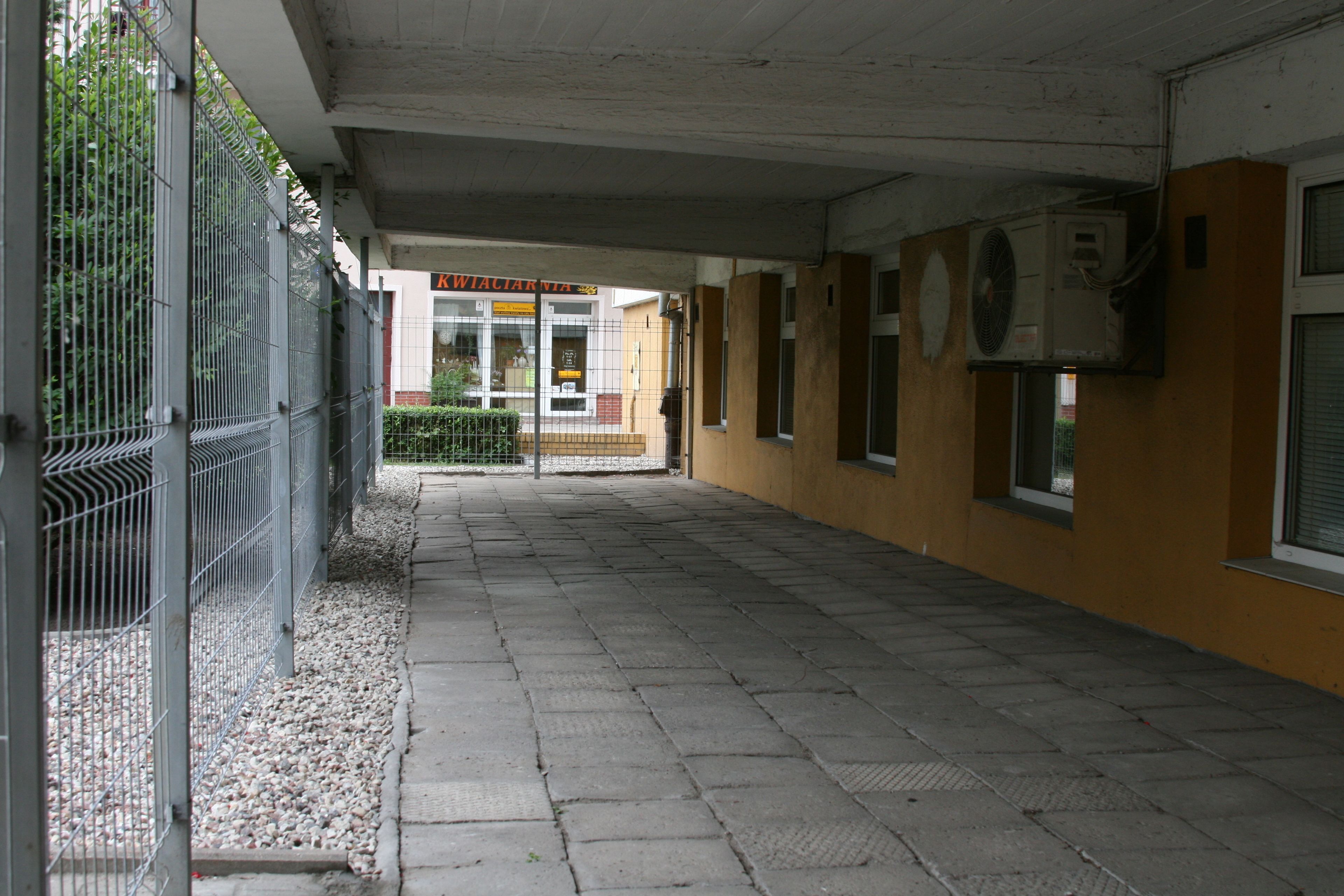 A corridor with a tiled floor, metal fence, and a building entrance with a sign.
