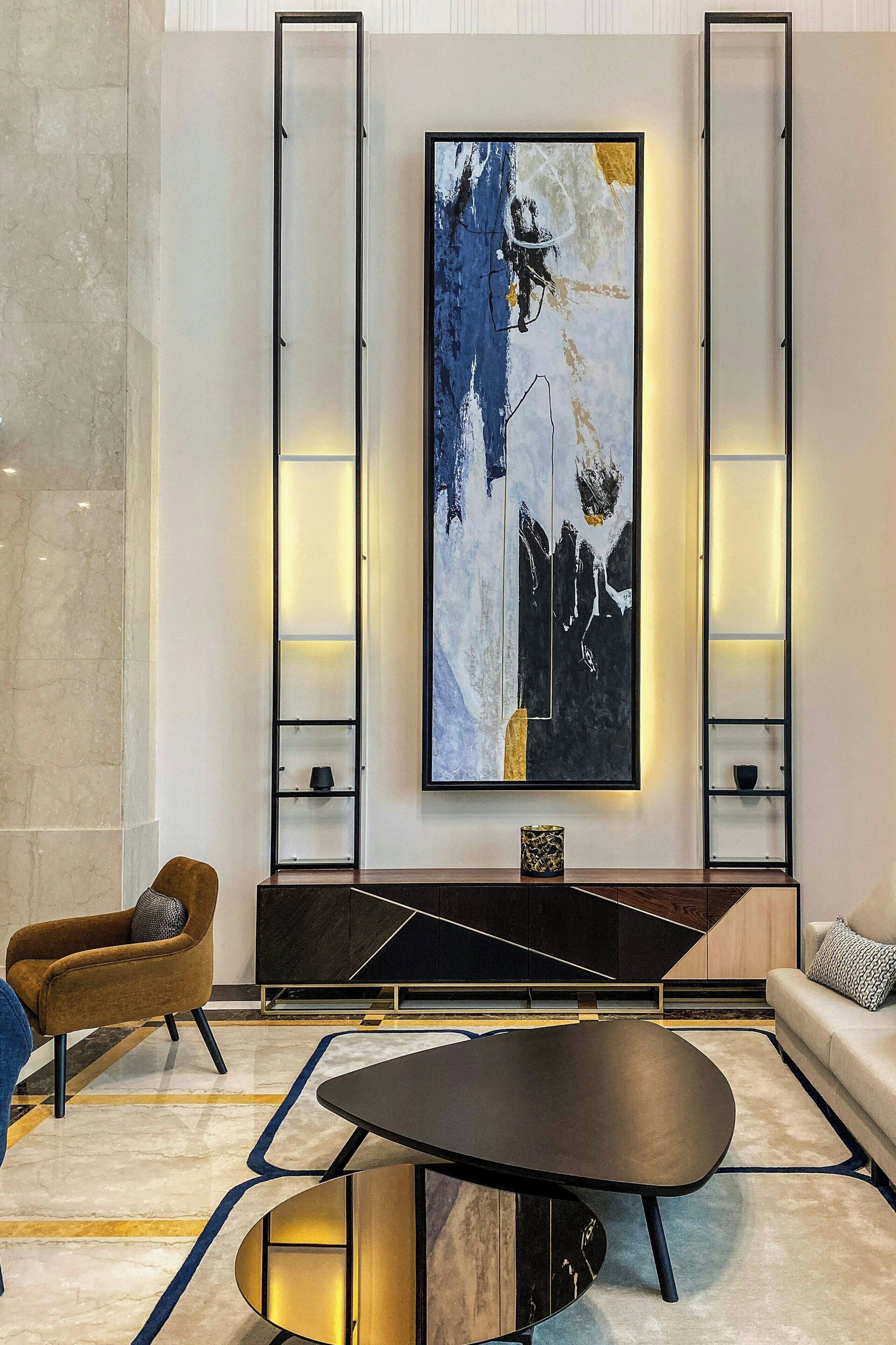 Una sala de estar moderna con un cuadro abstracto grande, un sofá, una mesa de centro y un sillón marrón.