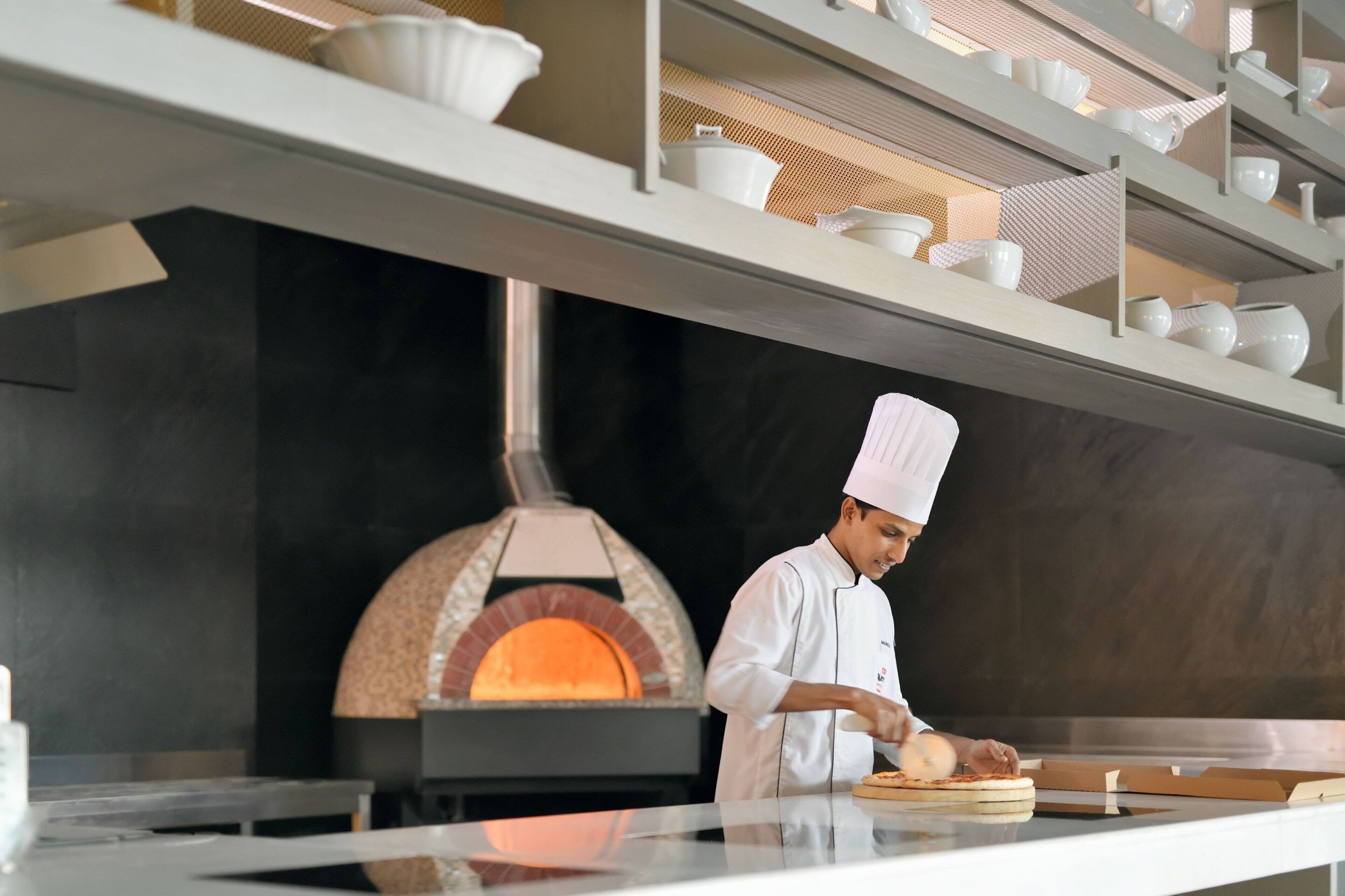 Ein Koch bereitet Pizza in einer modernen Küche mit einem Backofen aus Ziegelsteinen zu.