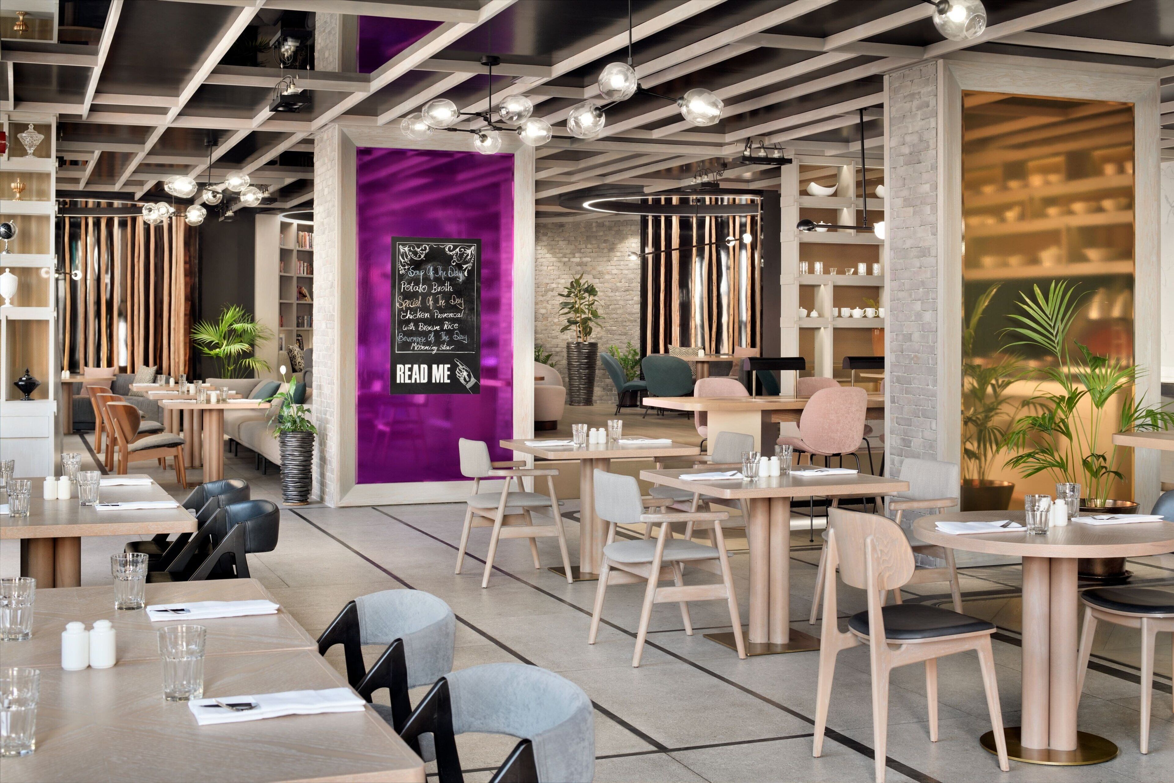 Un restaurante moderno con mesas redondas, sillas de madera y una pared de acento morada con un menú en pizarra.