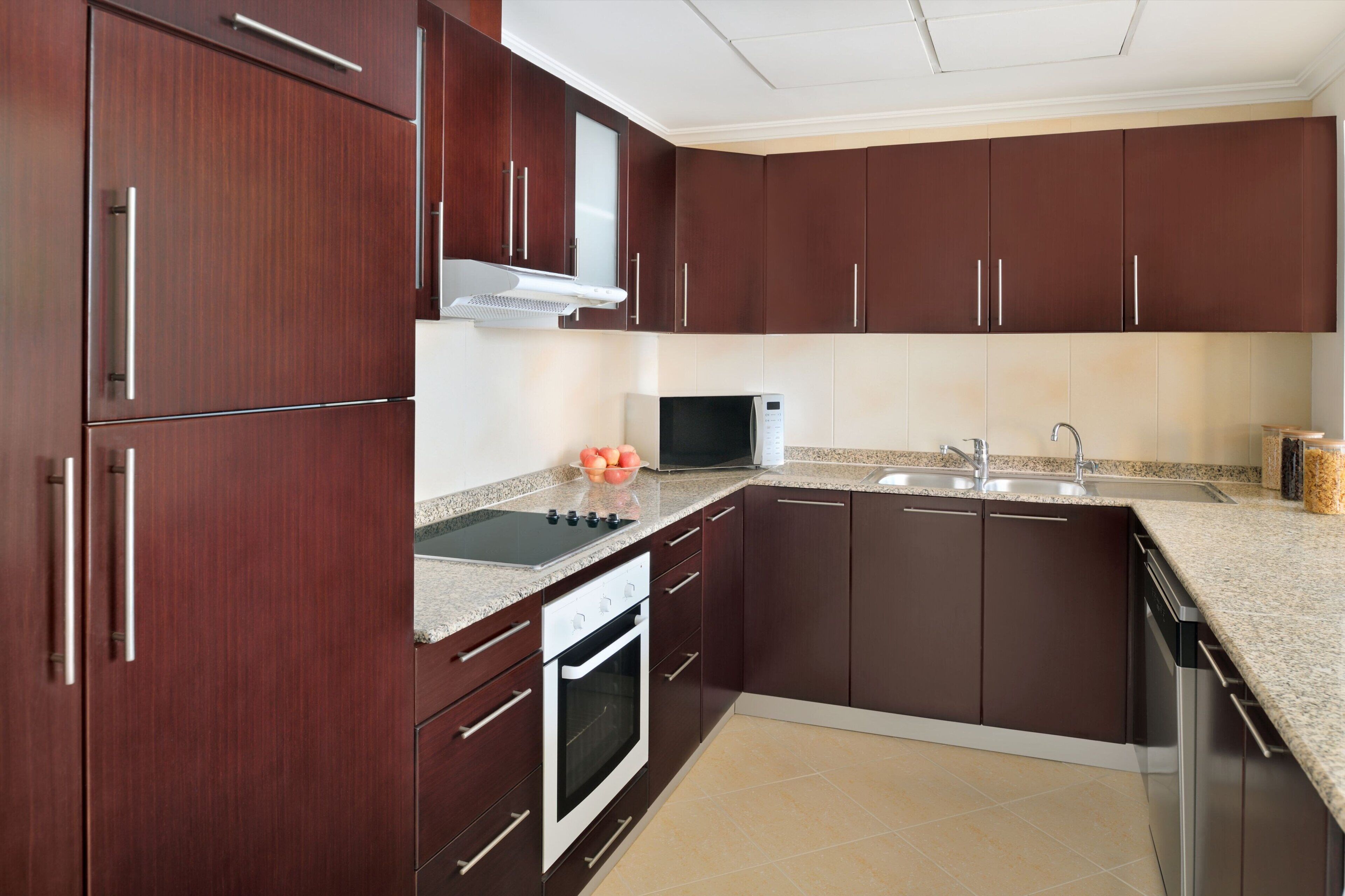 A modern kitchen with dark brown cabinets, a stainless steel range hood, a microwave, a sink, and a dishwasher.