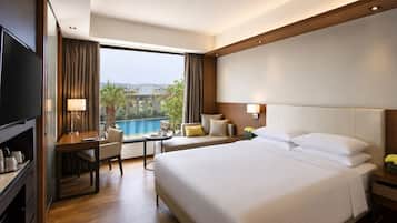 A hotel room with a large bed, a desk, a chair, a TV, and a view of a swimming pool.