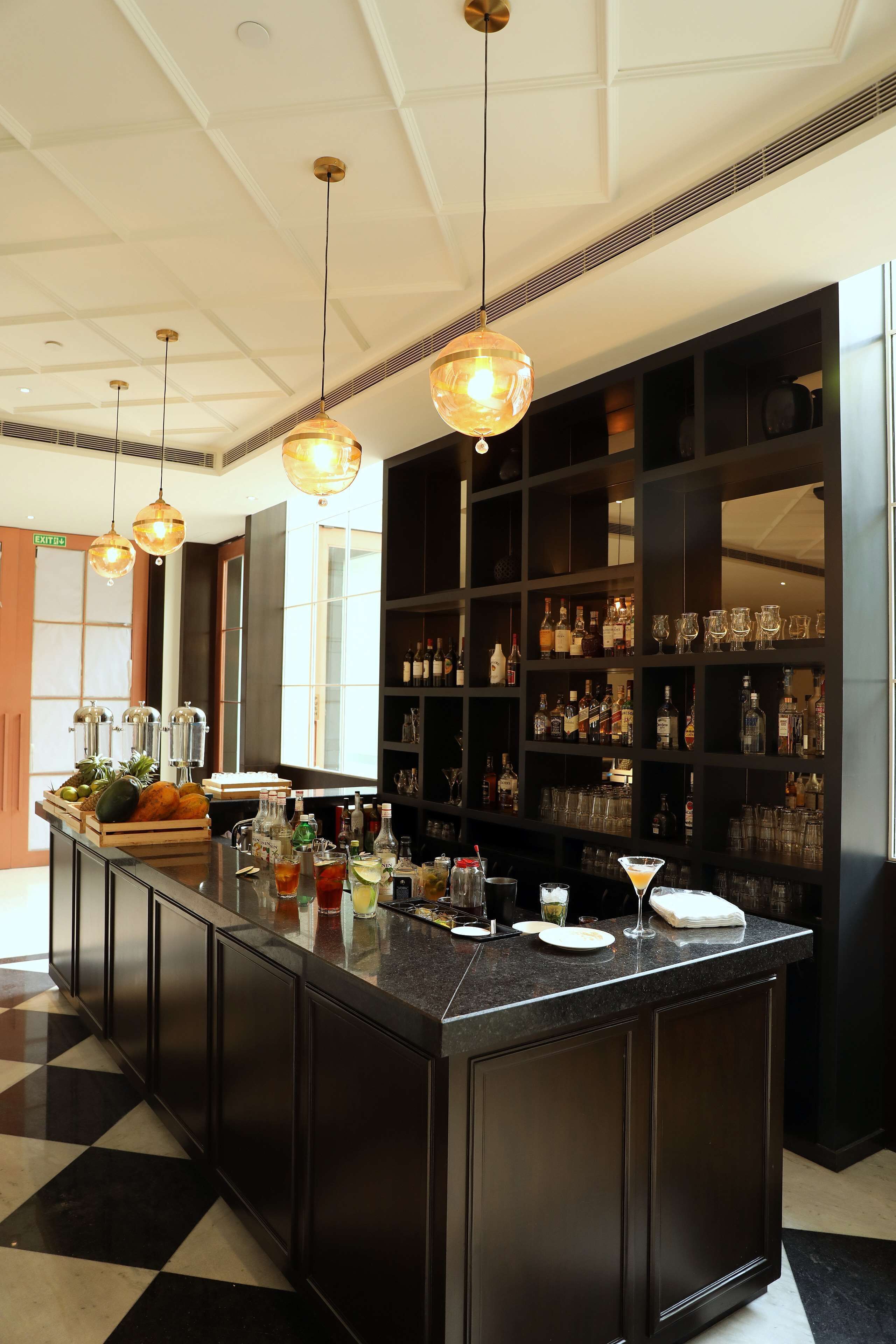 A bar area with a central island, shelves with bottles and glasses, and pendant lighting.