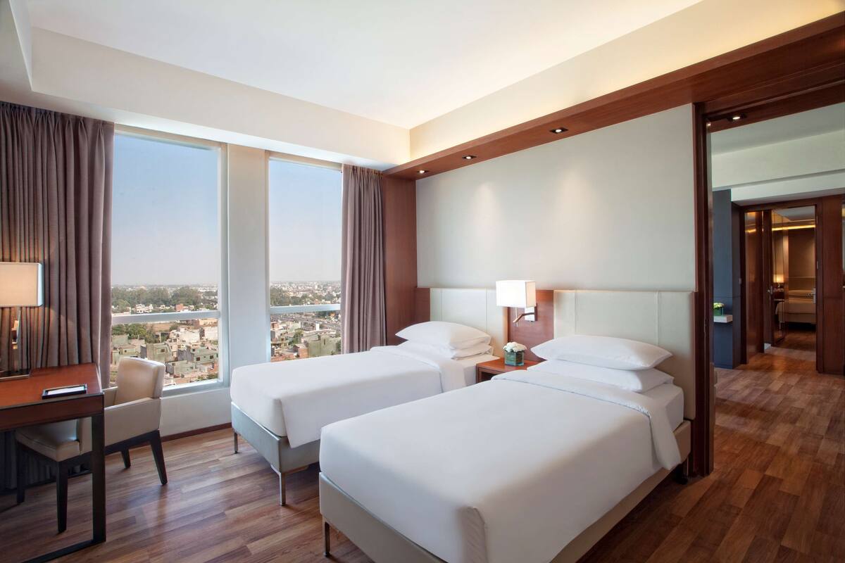 A hotel room with two beds, a desk, and a view of the city.