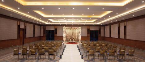 A large conference room with rows of chairs facing a stage, a carpeted floor, and a ceiling with recessed lighting.