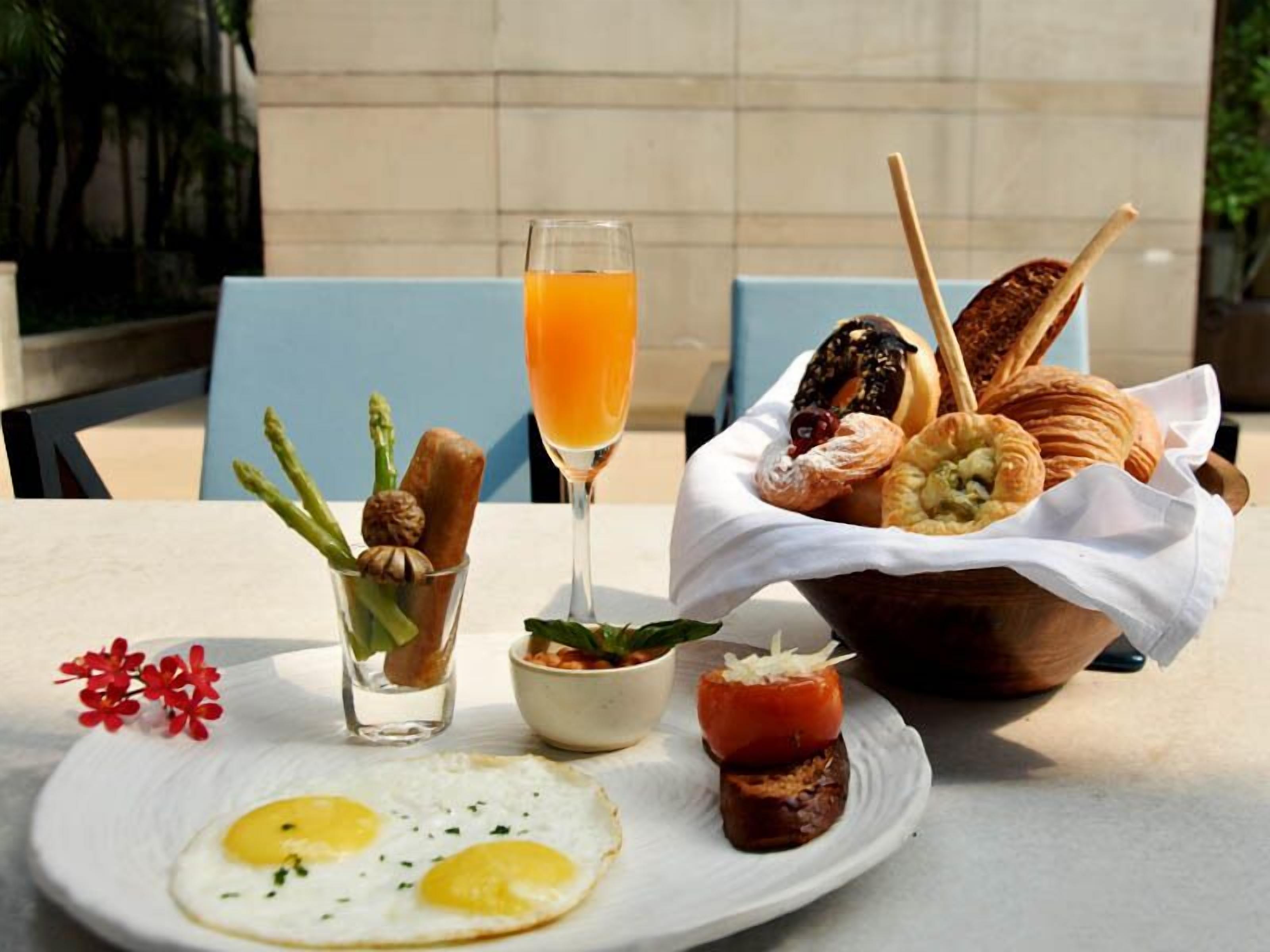 A breakfast setting with eggs, toast, pastries, and a glass of orange juice on a table.