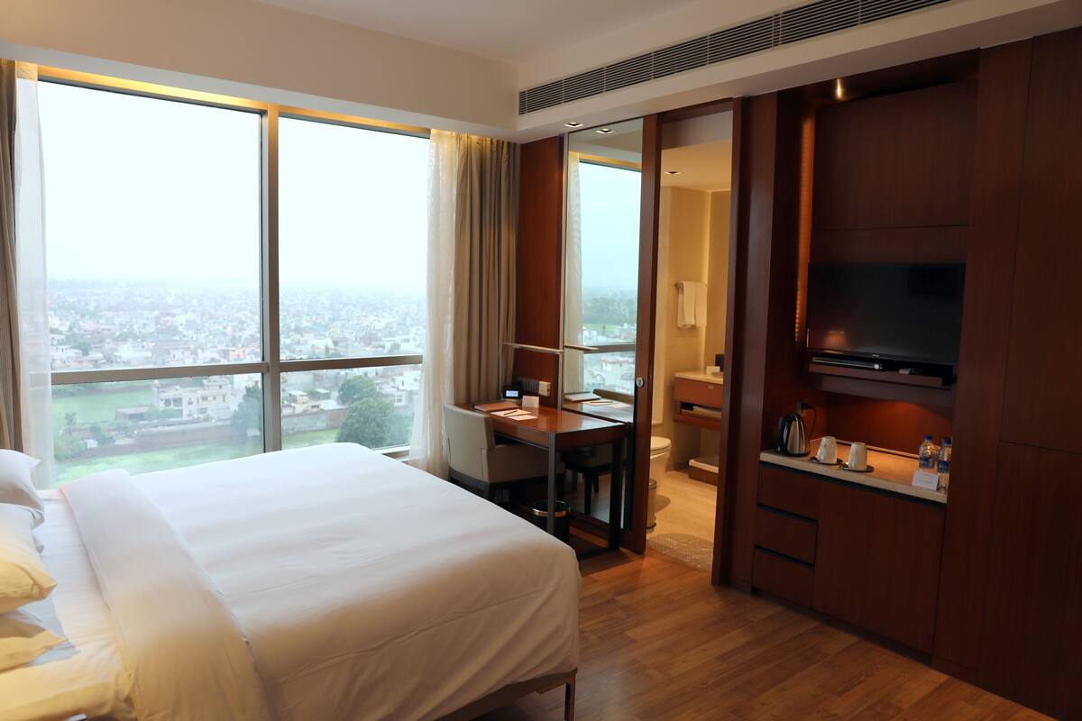 A hotel room with a bed, a desk, a television, and a view of the city.