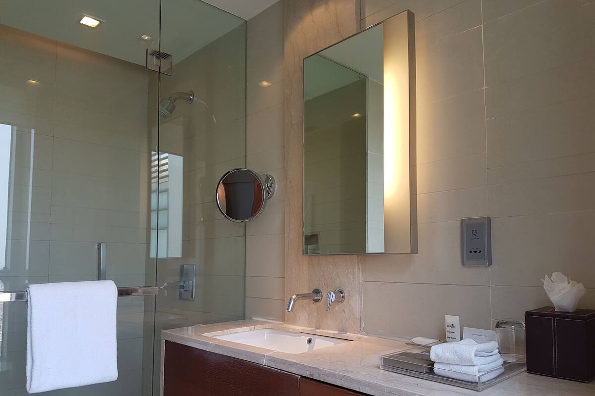A modern bathroom with a glass shower enclosure, a large mirror, a sink with a vanity, and a hair dryer.