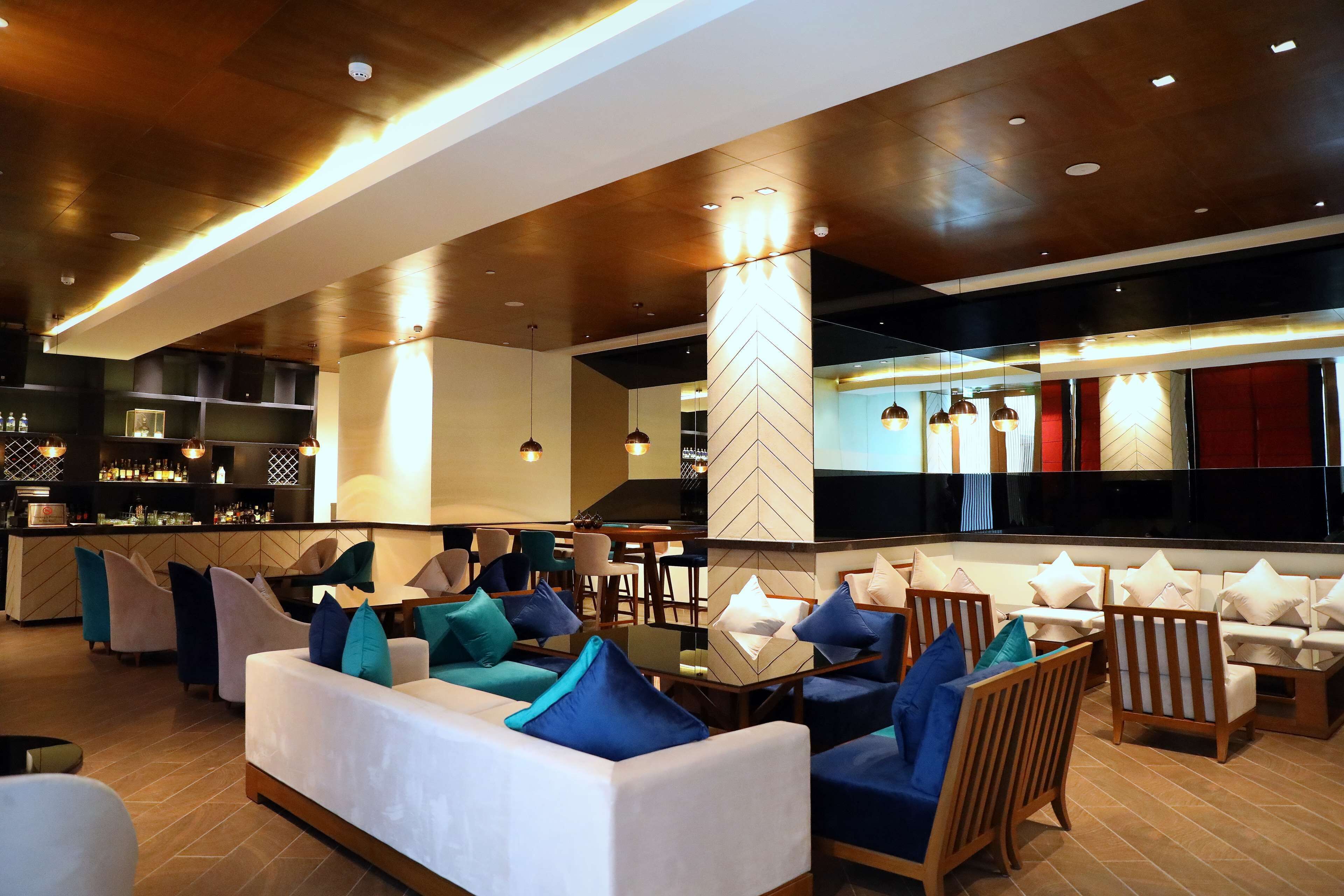Un moderno espacio de sala de estar con sofás y sillones, un bar y un pilar con estampado de tablero de ajedrez.