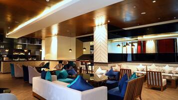 A modern lounge area with sofas and chairs, a bar, and a herringbone-patterned pillar.