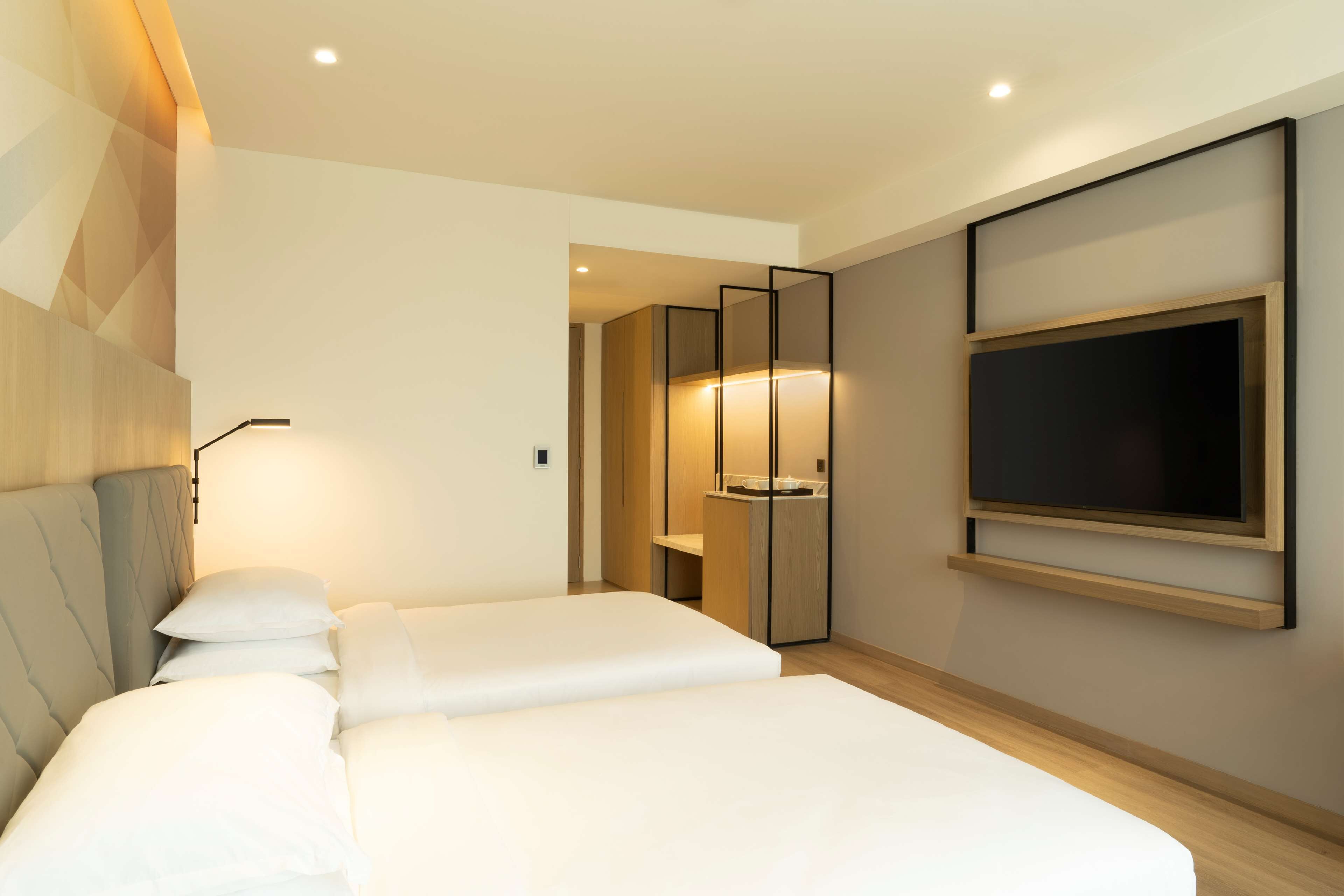 Ein modernes Hotelzimmer mit einem großen Bett, einem an der Wand montierten Fernseher und einer separaten Sitzecke mit Tisch und Stühlen.