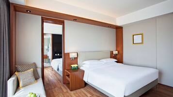 Habitación de hotel con cama, mesita de noche con lámpara, sofá con cojín y una pequeña mesa con manzanas.