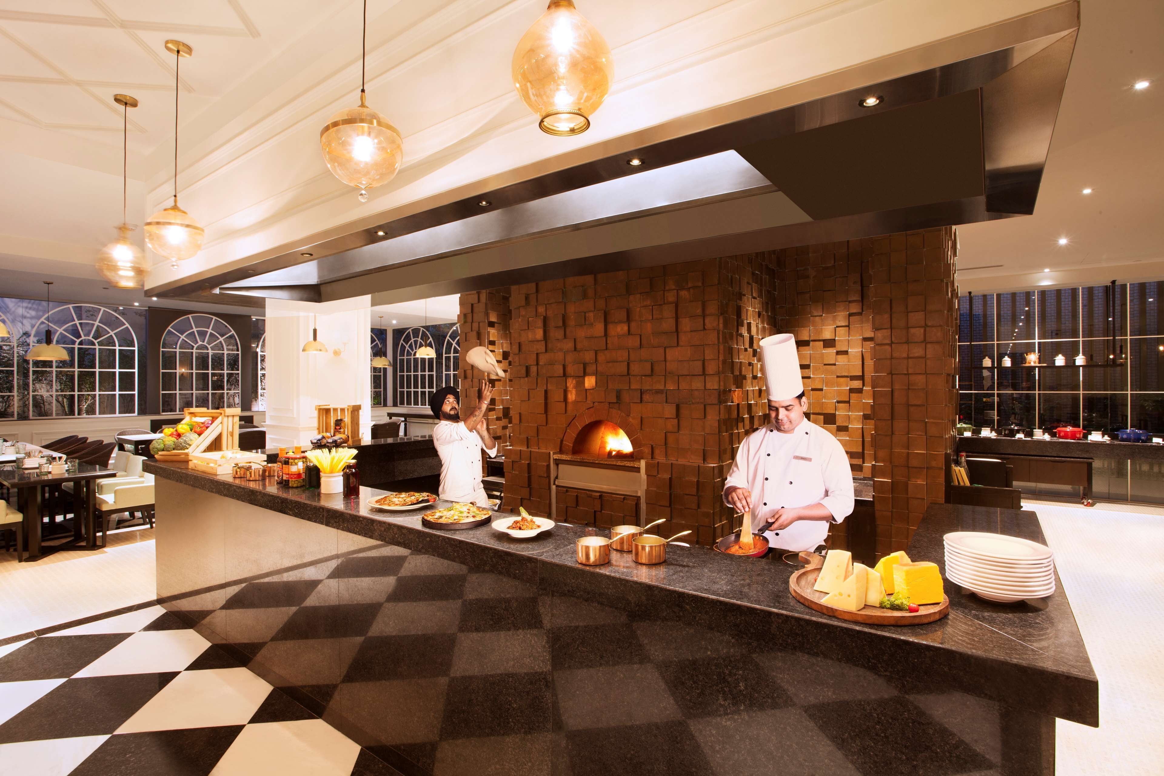A modern kitchen with chefs preparing food, a brick wall, and a checkered floor.