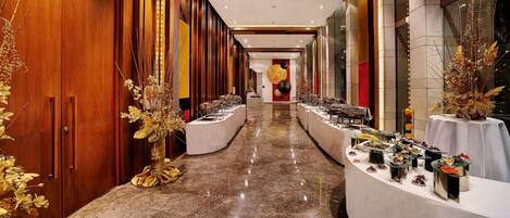 A corridor with a long buffet table, wooden paneling, and decorative golden foliage.