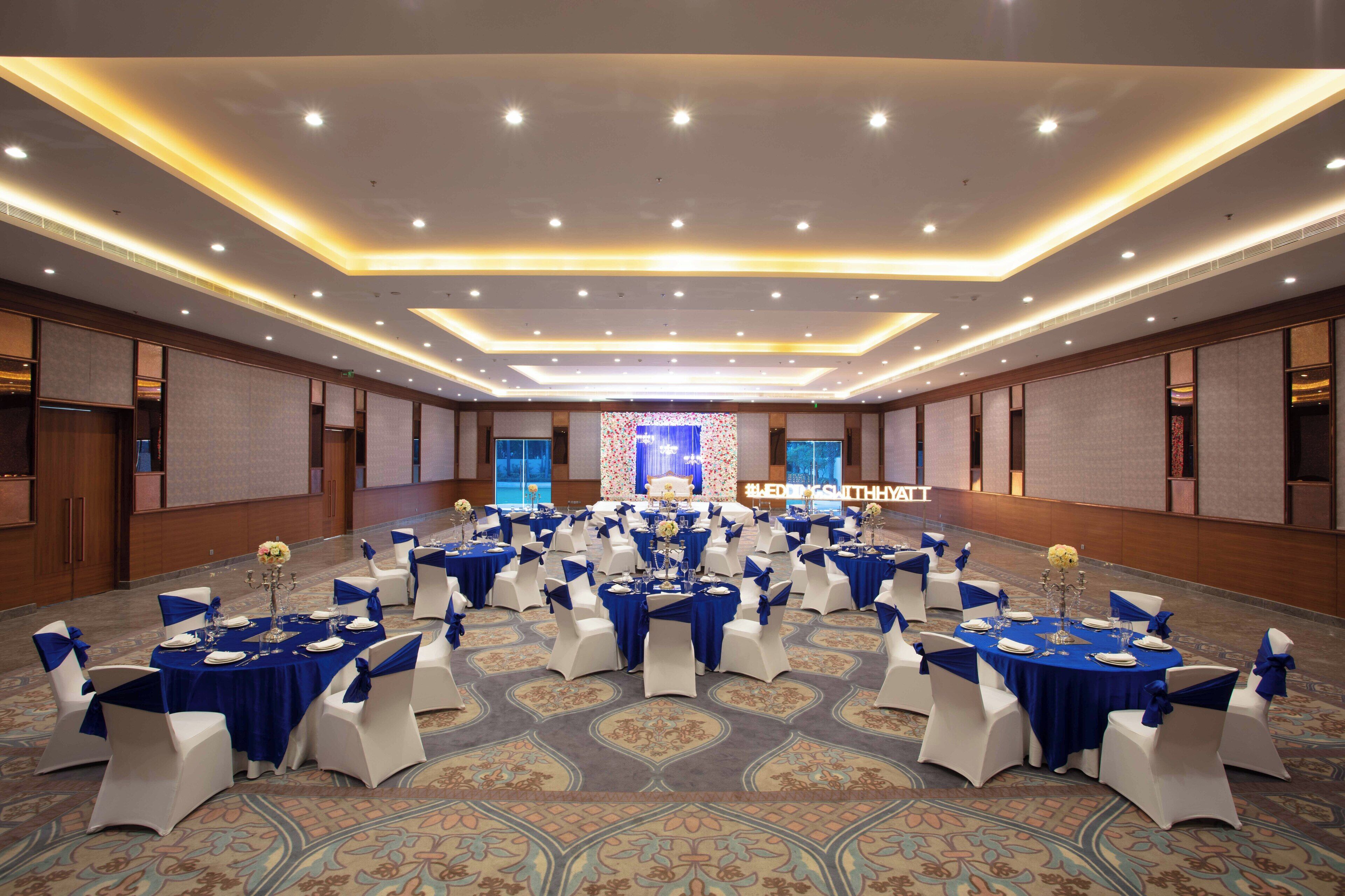 A banquet hall with round tables, white chairs, and blue tablecloths.
