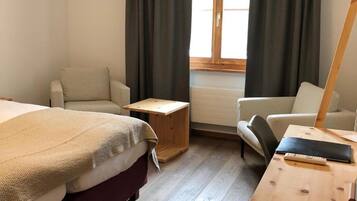 A bedroom with two beds, a desk, a chair, and a window with curtains.