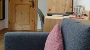 A room with a wooden door, a desk with a lamp, a chair, and a sofa with cushions. - Schorta's Hotel Alvetern (Scuol)