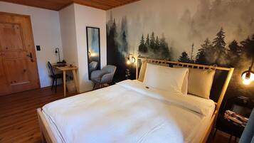 A bedroom with a bed, a desk, a chair, a mirror, and a wall mural.
