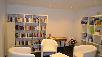 Una biblioteca con estanterías blancas, una mesa redonda de madera y sillas blancas.