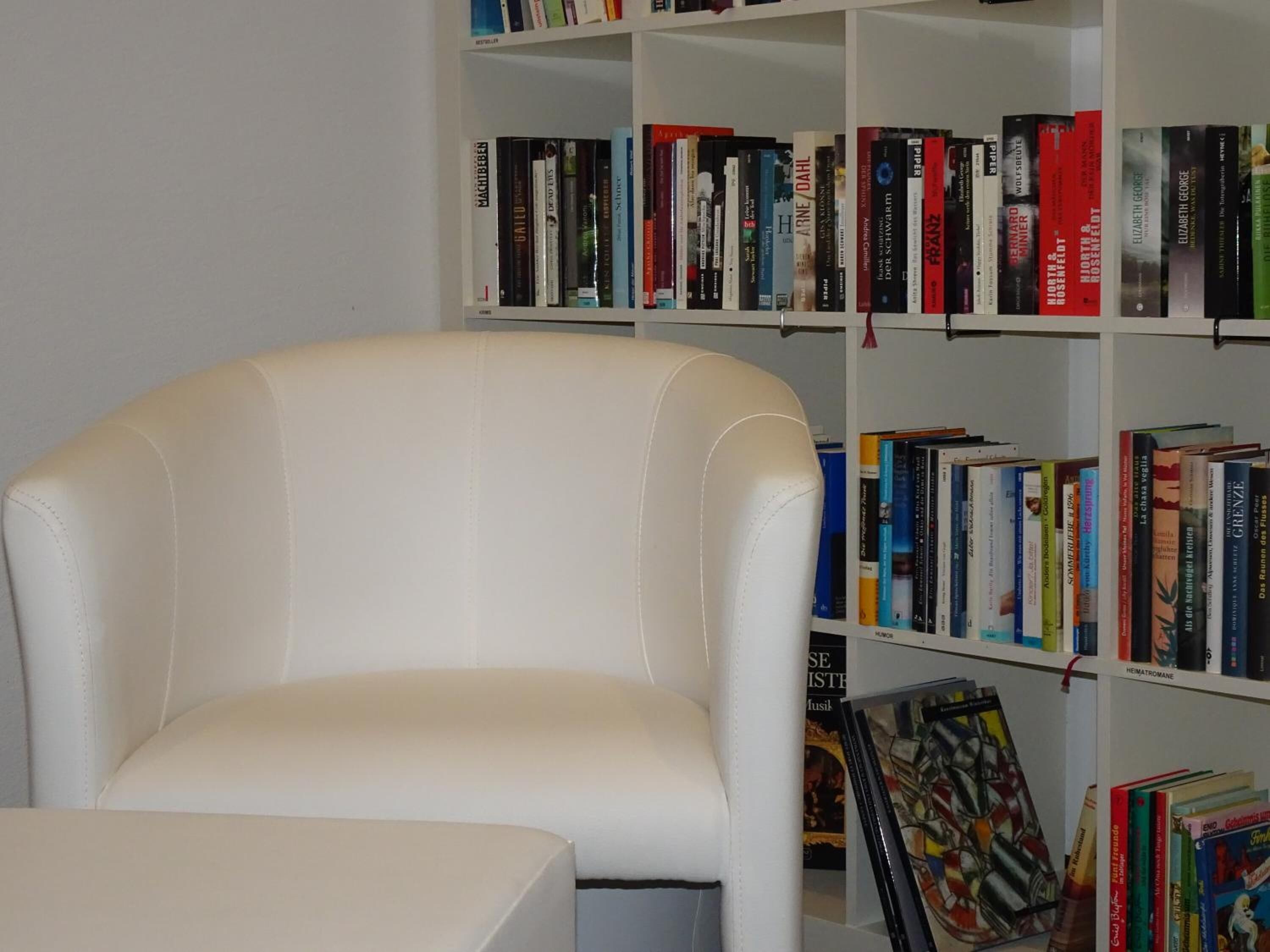 A white leather armchair in front of a bookshelf filled with books.