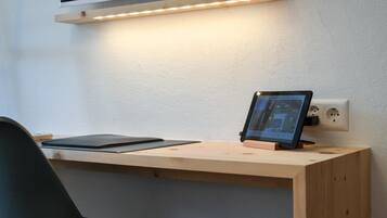 Un escritorio de madera con una tablet, una silla negra y un estante fijado a la pared sobre un enchufe.