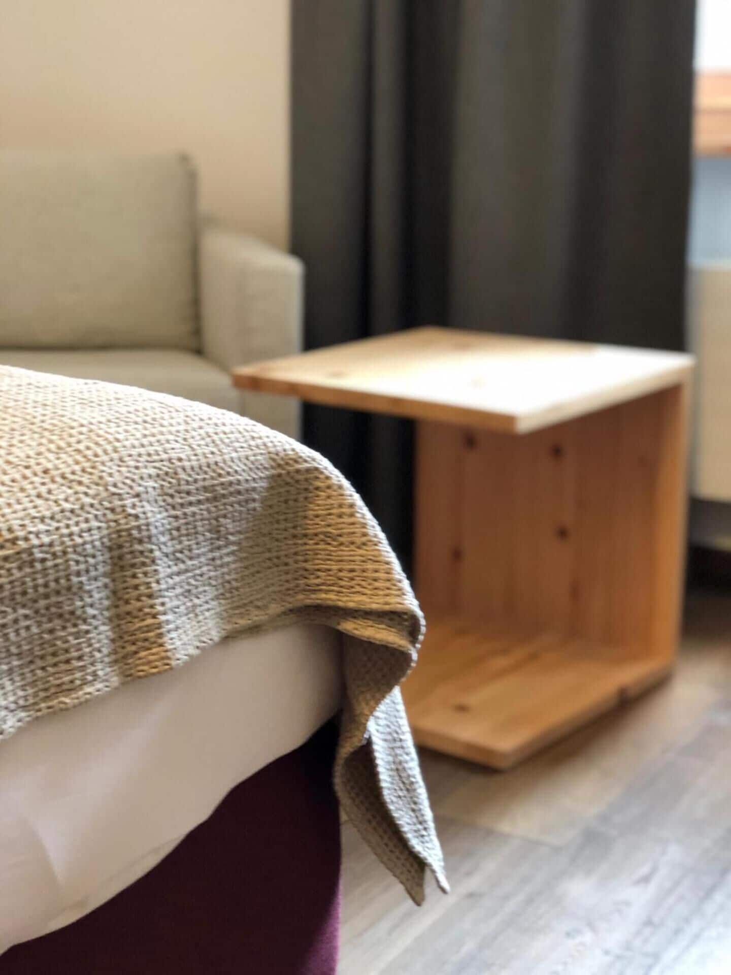 Ein Bett mit einer gestrickten Decke, ein Holfnachtisch und ein Sofa in einem Zimmer mit Holzboden.