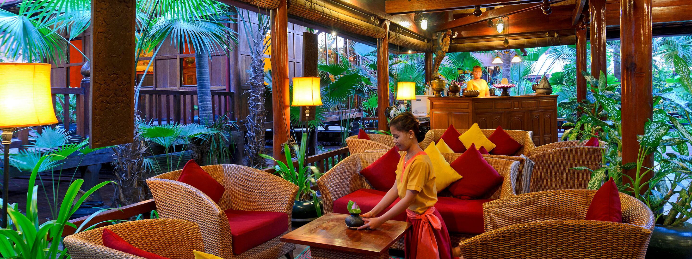A tropical-themed restaurant interior with wicker furniture, red cushions, and lush greenery.
