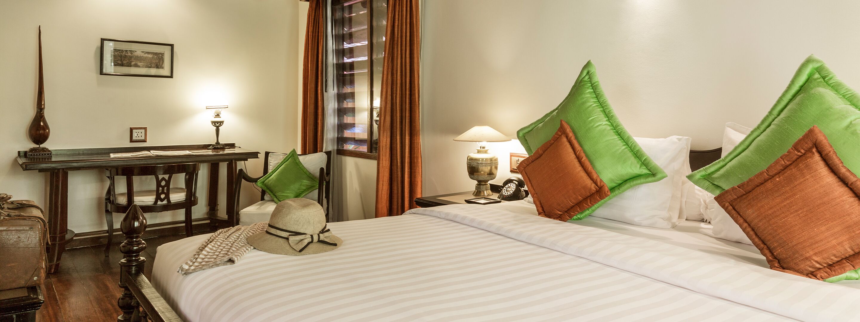 Habitación de hotel con cama, escritorio, lámpara, reloj y un cuadro en la pared.
