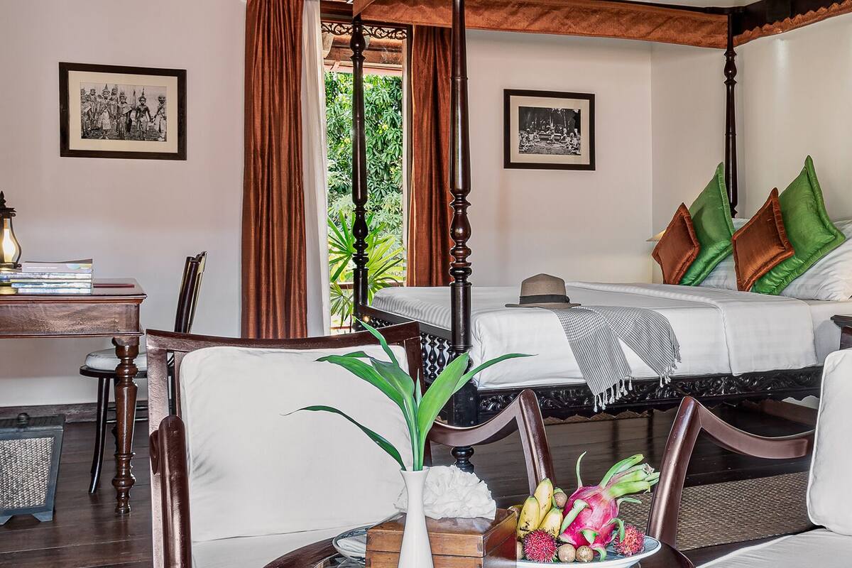 A four-poster bed with a canopy, a bedside table with a lamp, and a chair with a fruit bowl.