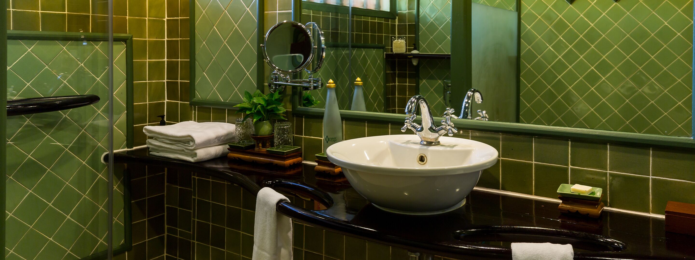 A bathroom with a white sink, green tiled walls, a mirror, and a towel rack.