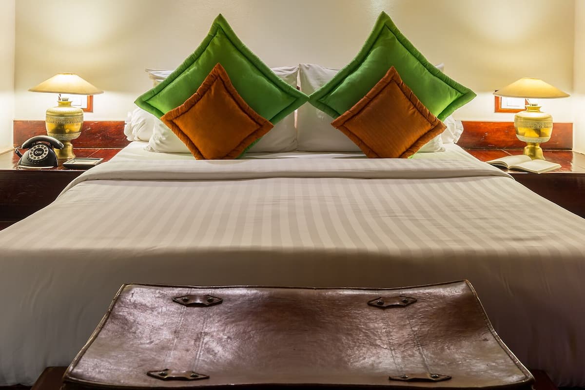 A hotel room with a large bed, two nightstands, a lamp on each, and a brown leather ottoman.