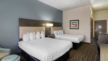 A hotel room with two beds, a desk, a chair, a trash bin, and a framed picture on the wall.