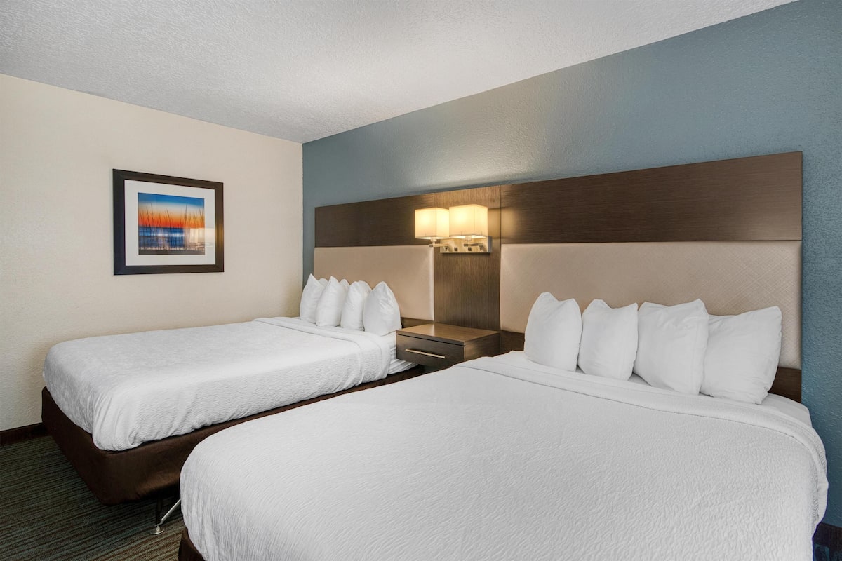 A hotel room with two single beds, a nightstand, a lamp, and a framed picture on the wall.