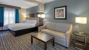 A hotel room with a bed, a sofa, a coffee table, and a small table with a lamp. - Best Western Waldo Inn and Suites (Waldo)