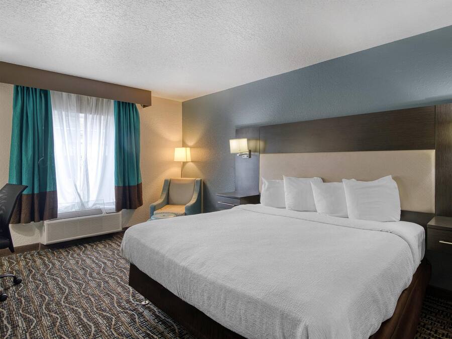 Una habitación de hotel con una cama grande, un escritorio, una silla, una lámpara y una ventana con cortinas.