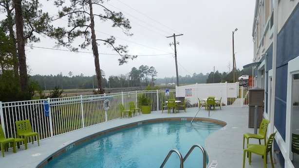 A swimming pool with a metal ladder, surrounded by a white fence and green chairs. - Best Western Waldo Inn and Suites (Waldo)