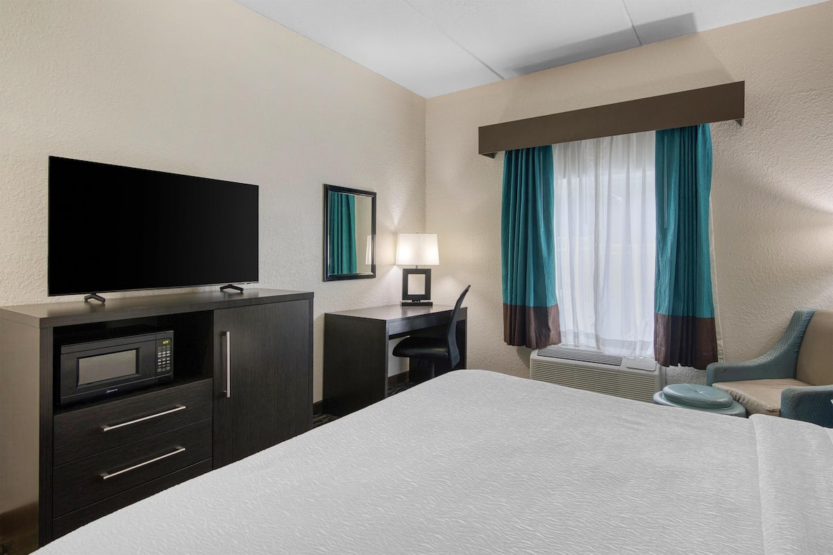 A hotel room with a bed, a desk, a television, a microwave, and a window with curtains.