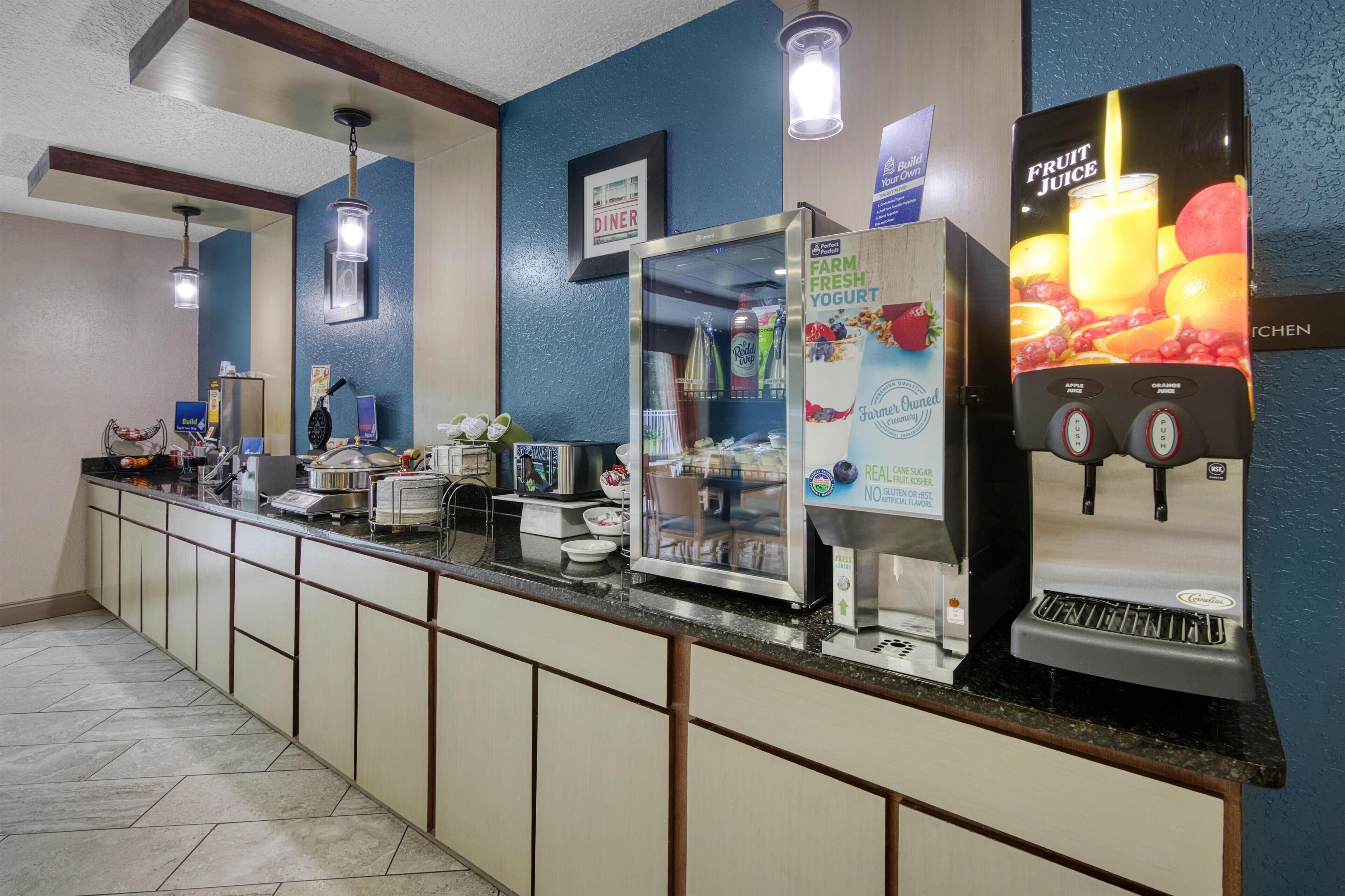 Een hotel receptie met een zelfbedieningsdrankstation, een koelkast en een bord dat een eetruimte aangeeft.