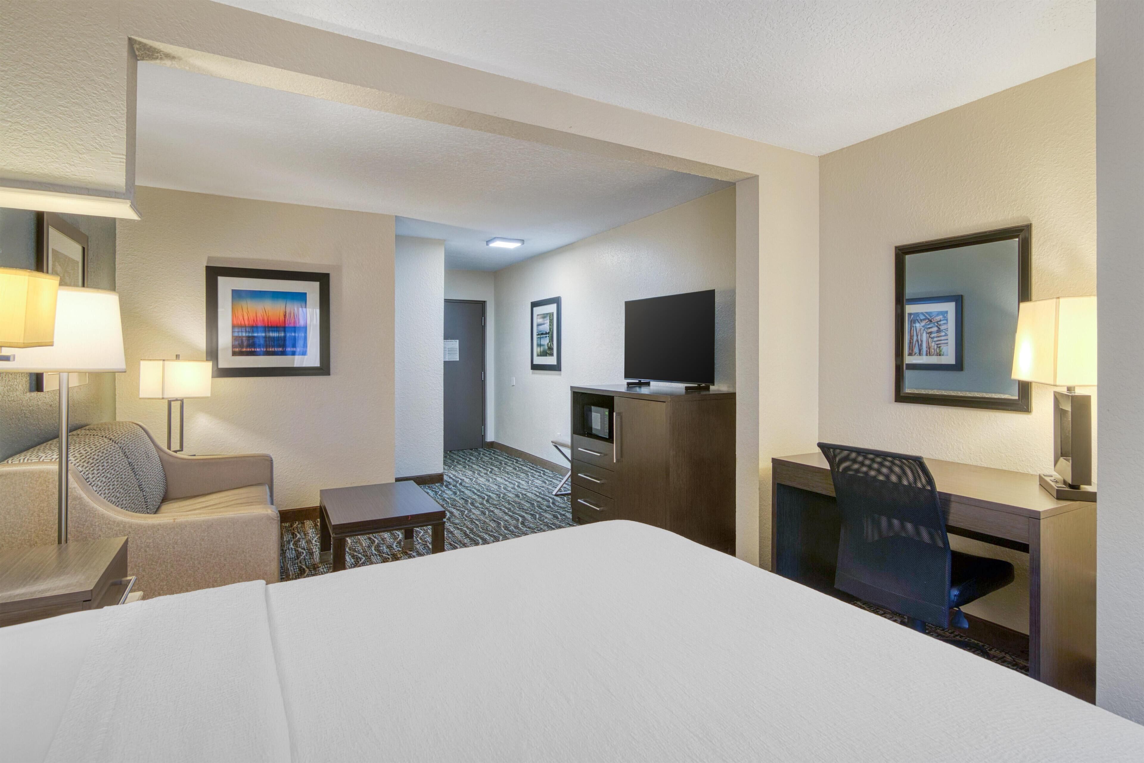 A hotel room with a bed, a desk, a chair, a TV, and a lamp.