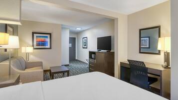 A hotel room with a bed, a desk, a chair, a TV, and a lamp.