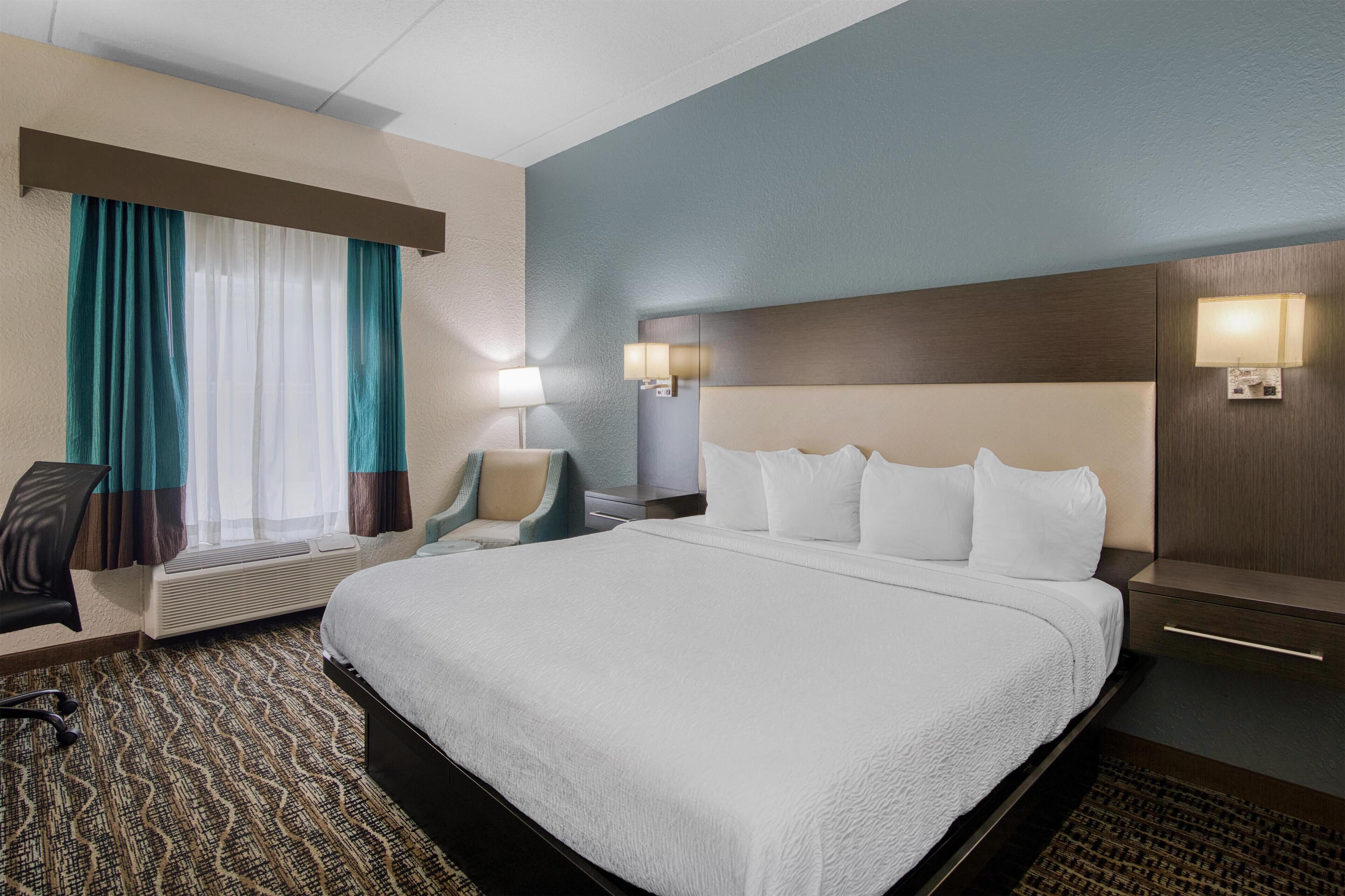 Een hotelkamer met een groot bed, een bureau, een stoel en een raam met gordijnen.