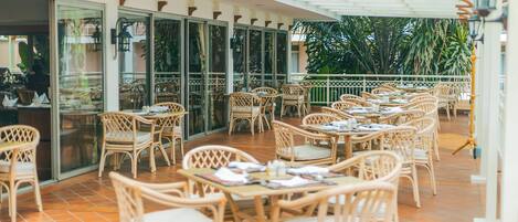 An outdoor cafe with wicker furniture and glass doors leading to the interior.