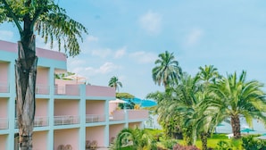 A multi-story hotel with balconies, a well-maintained lawn, and palm trees.