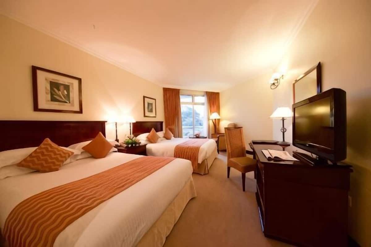 Habitación de hotel con dos camas, un escritorio con televisor y una ventana con cortinas.