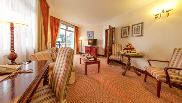 Une chambre d’hôtel équipée d’un canapé, de fauteuils, d’une table à manger, d’un téléviseur et de tableaux encadrés au mur.