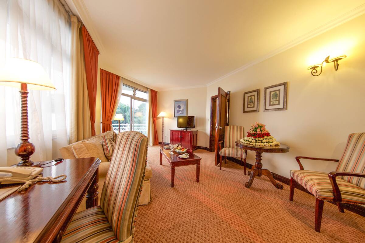 Habitación de hotel con sofá, sillones, una mesa de comedor, televisor y cuadros en la pared.