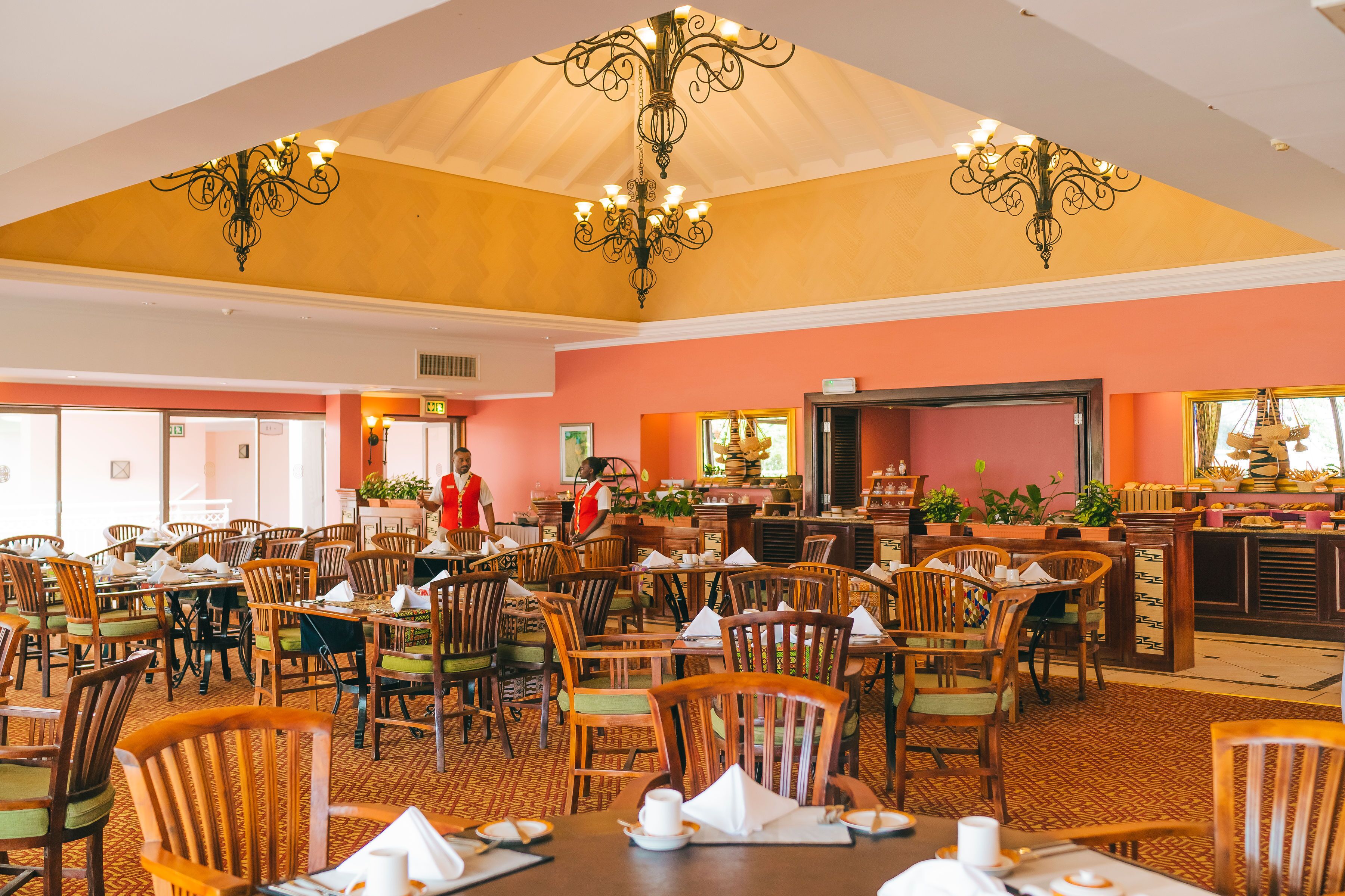 A spacious dining area with wooden tables and chairs, a central bar, and a chandelier.