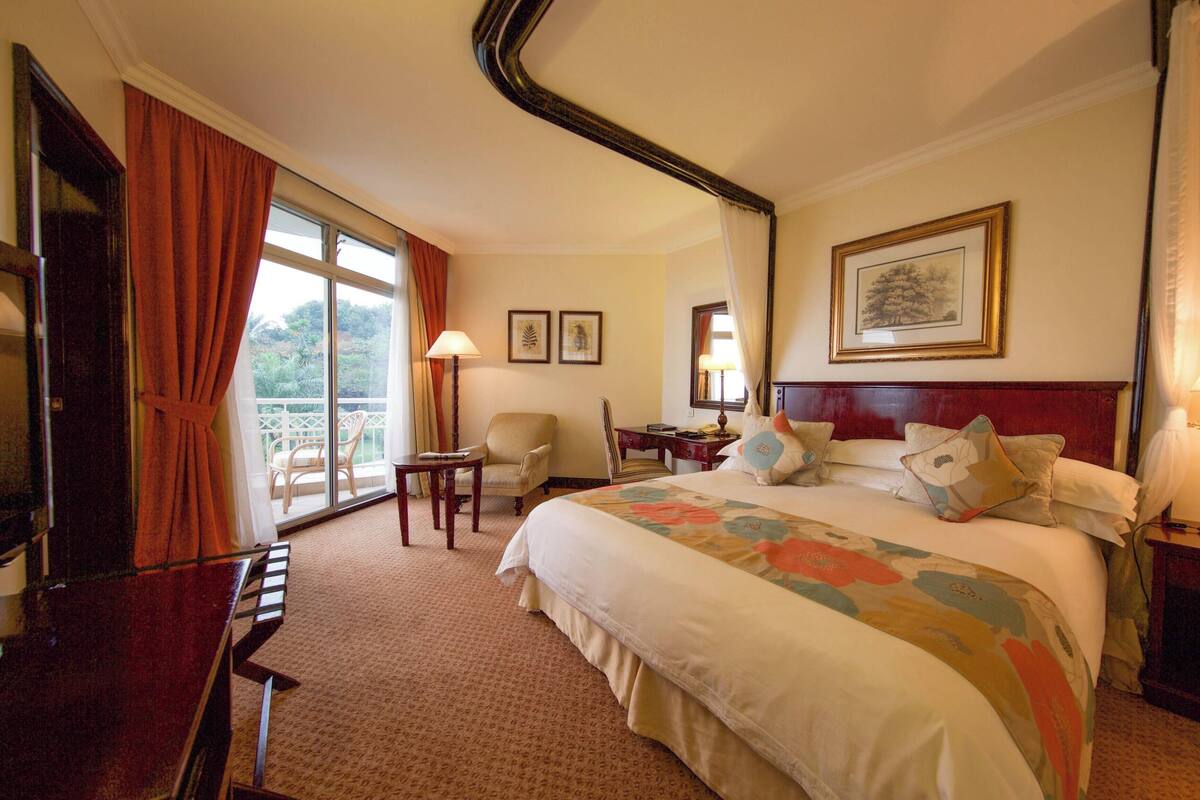 Habitación de hotel con cama, escritorio, silla, televisor y ventana con cortinas.
