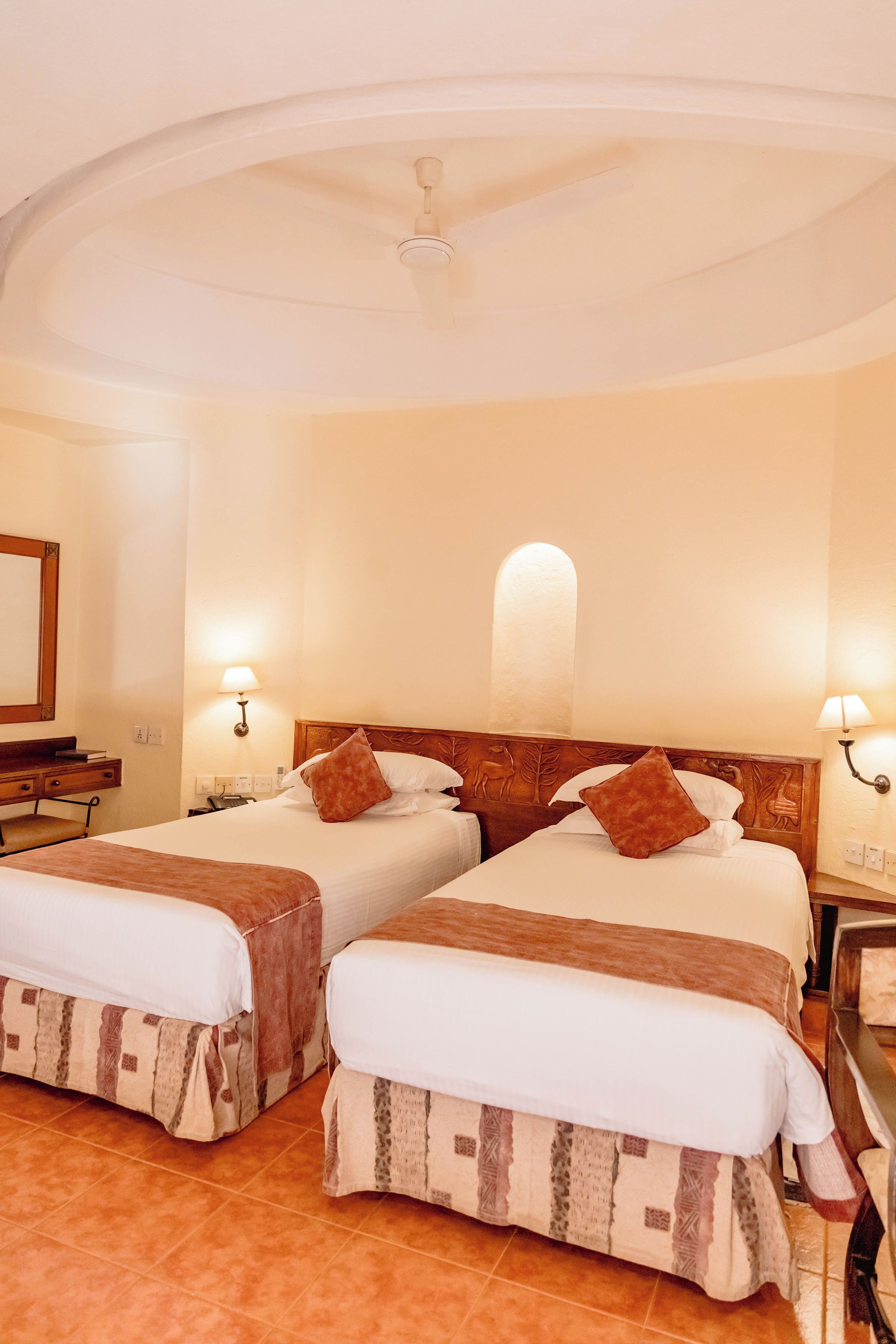 A hotel room with two beds, a desk, and a mirror.
