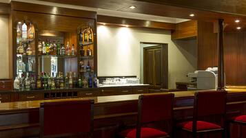 Zona de bar con mostradores de madera, sillas acolchadas rojas y estanterías llenas de botellas de licores.